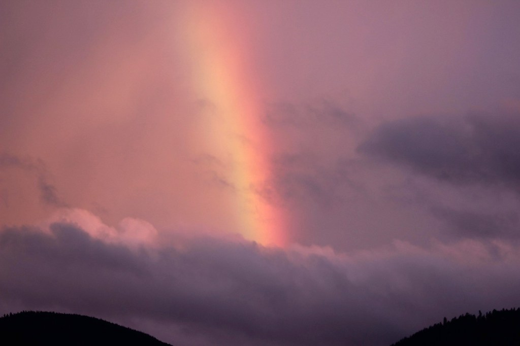 Photo, bright broad rainbow, in a stormy sky, above silhouetted rolling hills, image by Udo Voigt, on Pixabay, slightly modified.