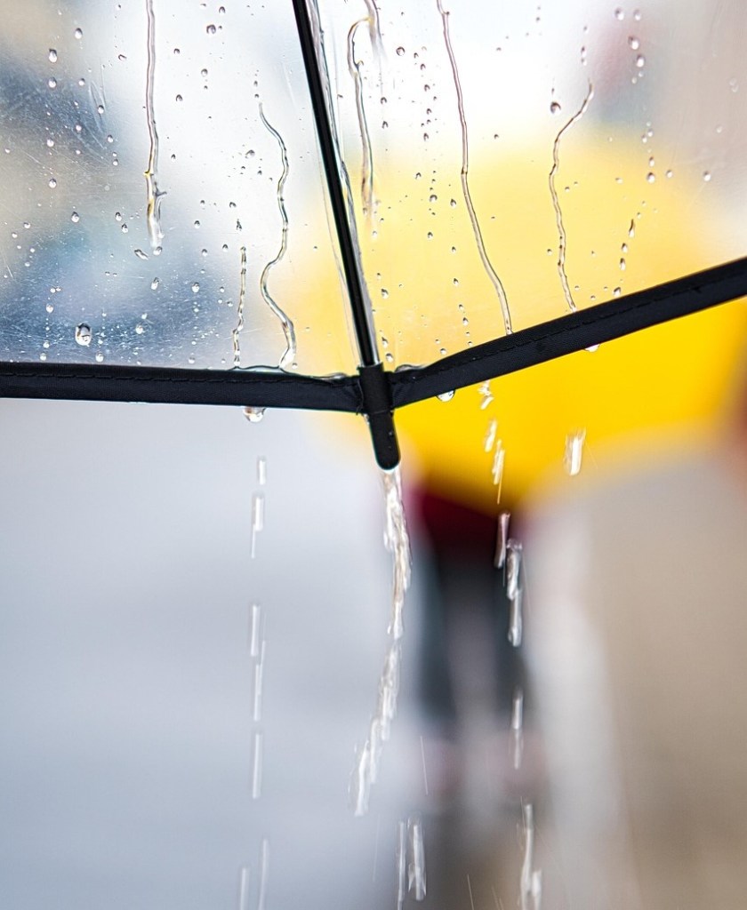 Photo: rainy day umbrella, looking through a clear umbrella at someone walking ahead of us with a yellow umbrella, image by anrica, on Pixabay, modified